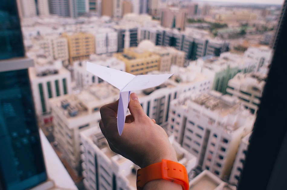 Eine Hand die einen Papierflieger hält, im Hintergrund sind Hochhäuser zu sehen