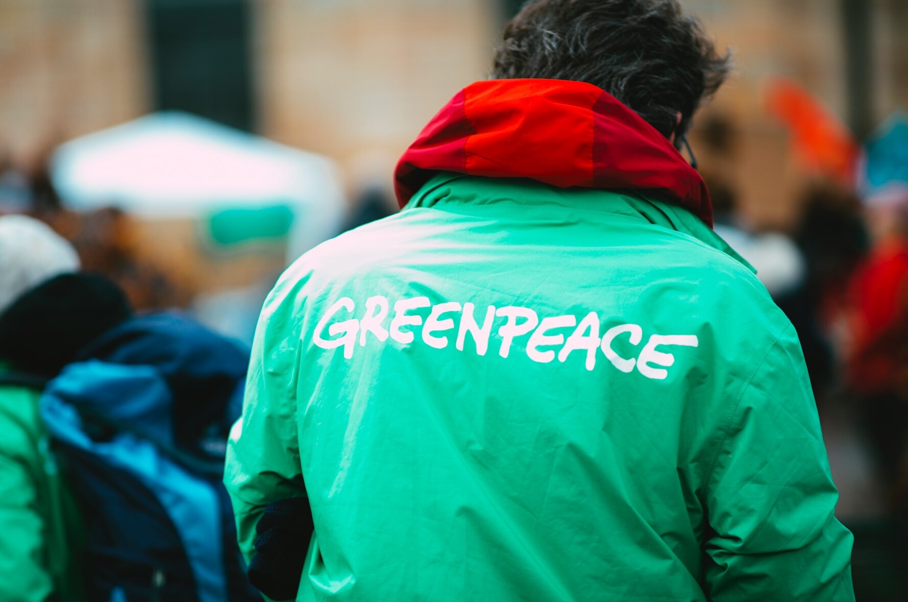 Ein Mann von hinten, auf dessen grüner Jacke "Greenpeace" steht